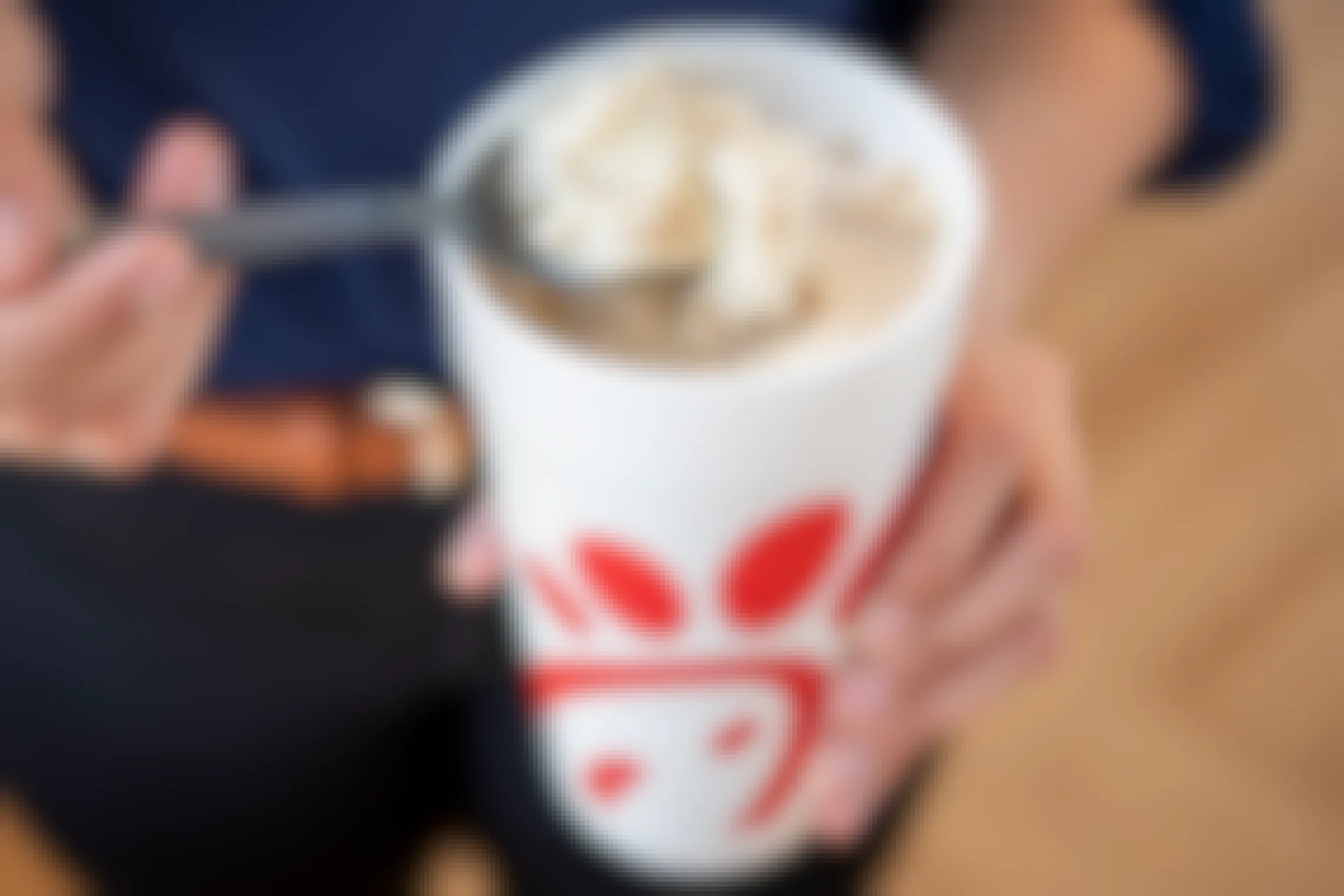 A person using a spoon to scoop ice cream from a root beer float in a Chick-fil-a cup.