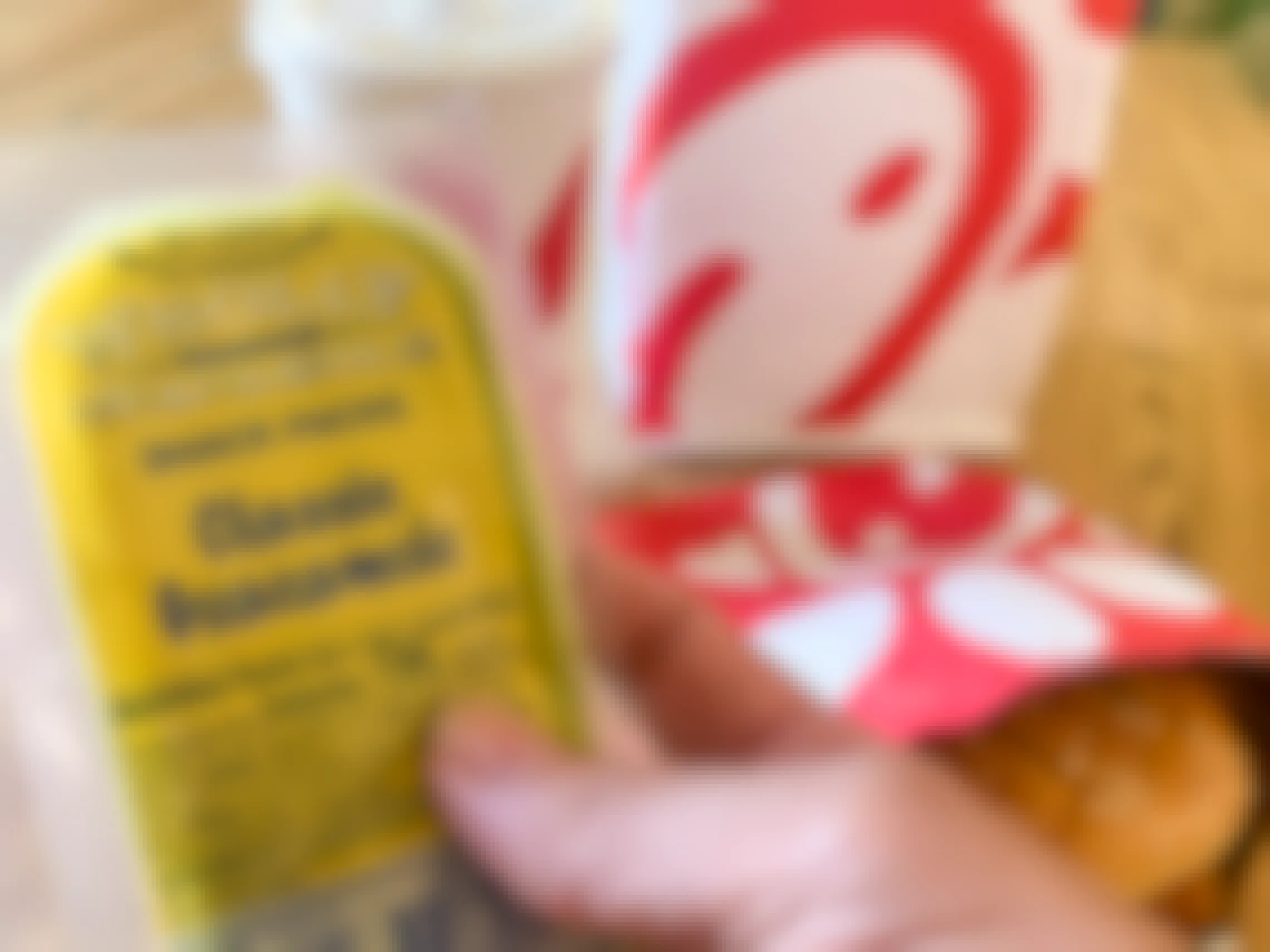 A person's hand holding a snack-pack-sized classic Guacamole next to a Chick-fil-A sandwich and drink.