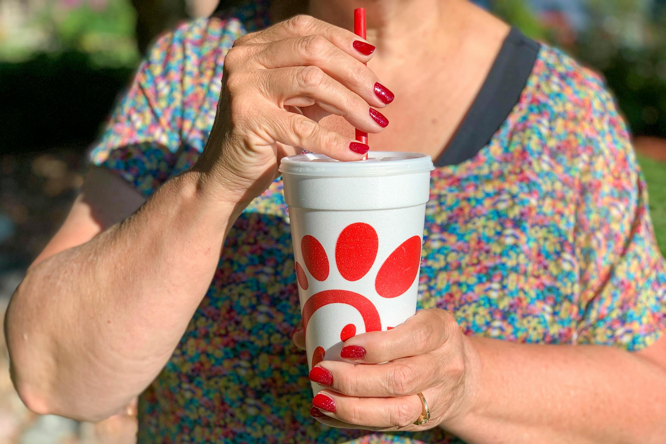 A senior-aged woman drinking soda from a Chick-fil-A drink cup.