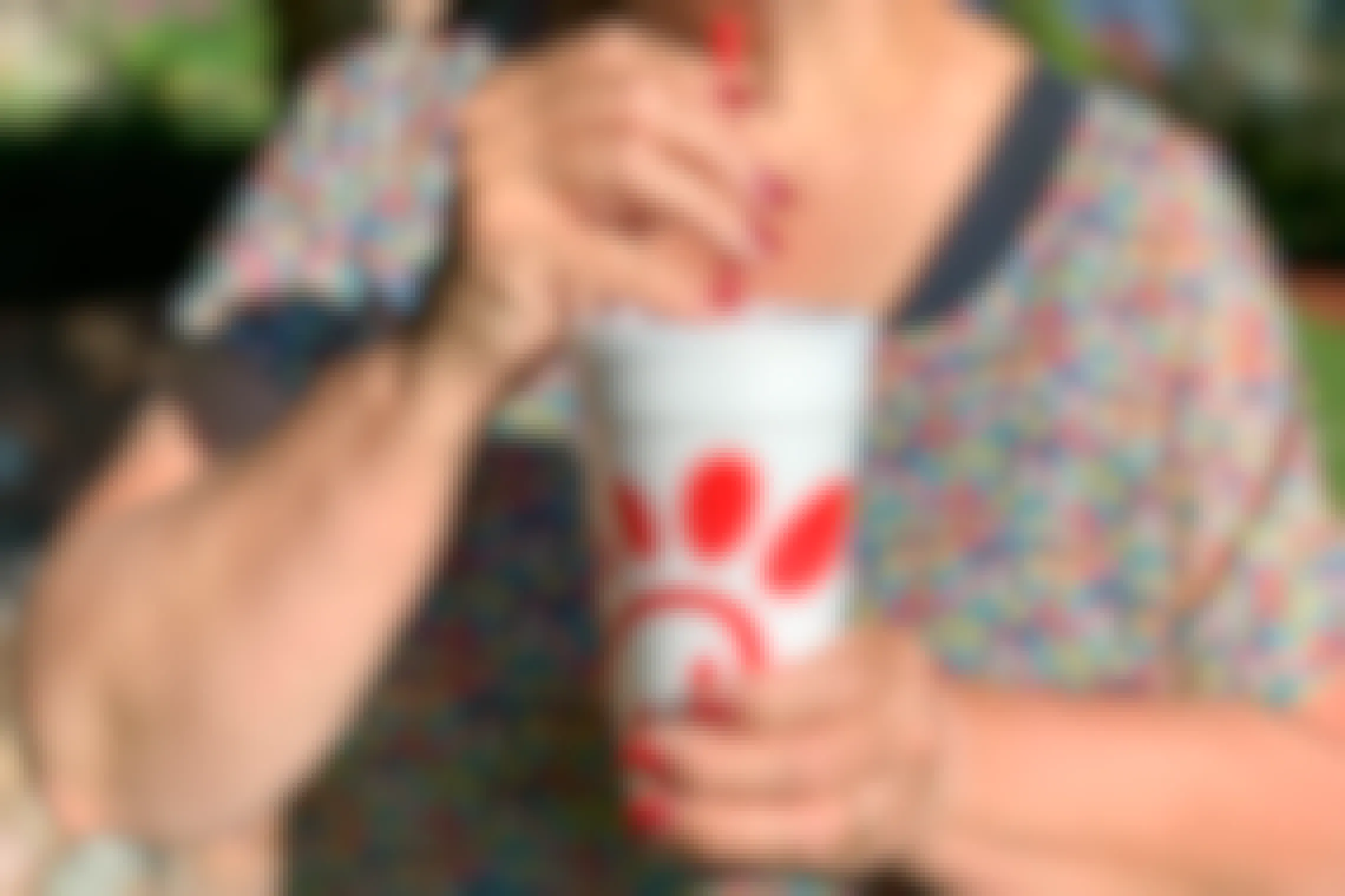 A senior-aged woman drinking soda from a Chick-fil-A drink cup.