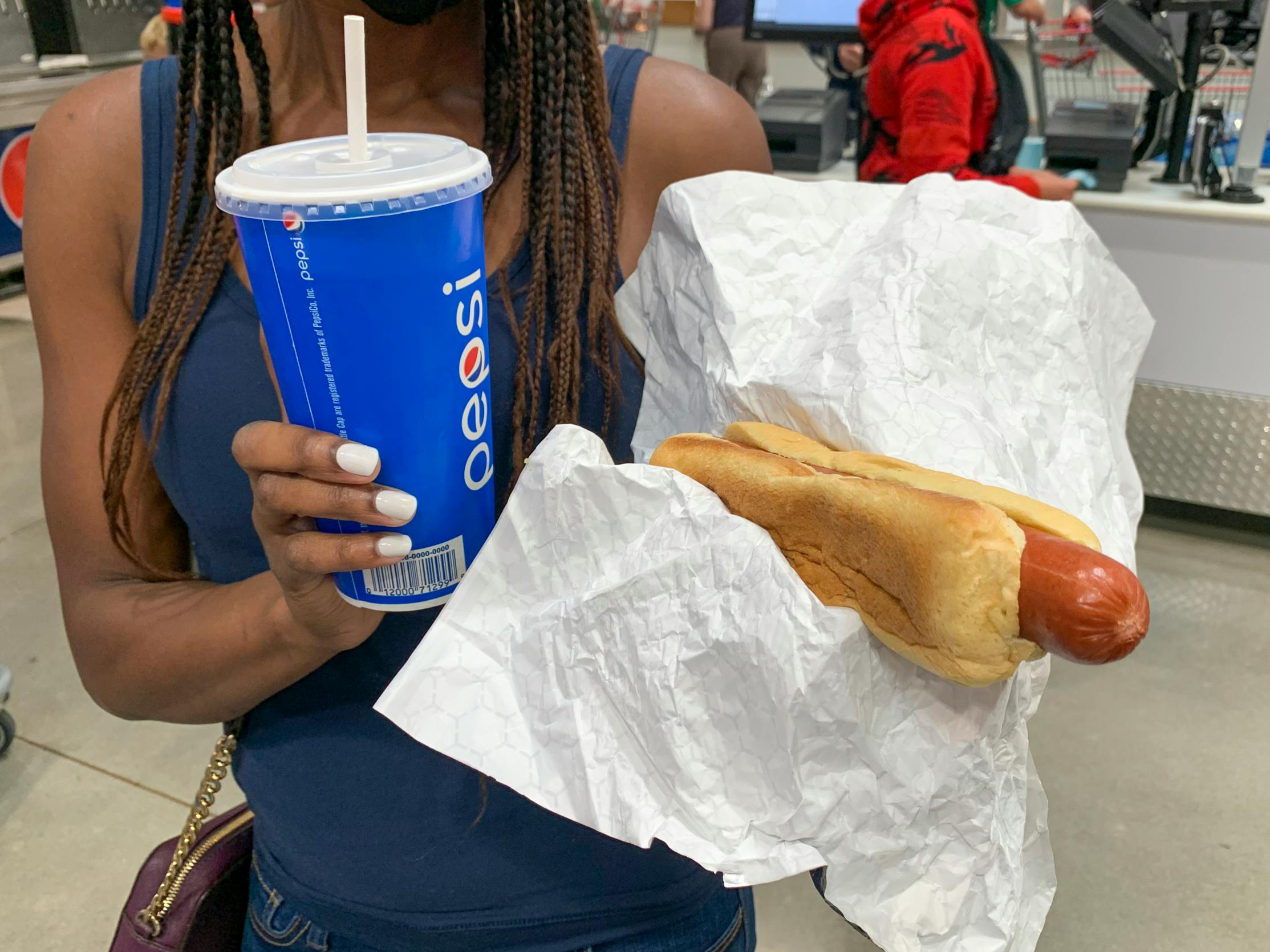 A woman holding a beverage cup and a hotdog near the Costco food court.