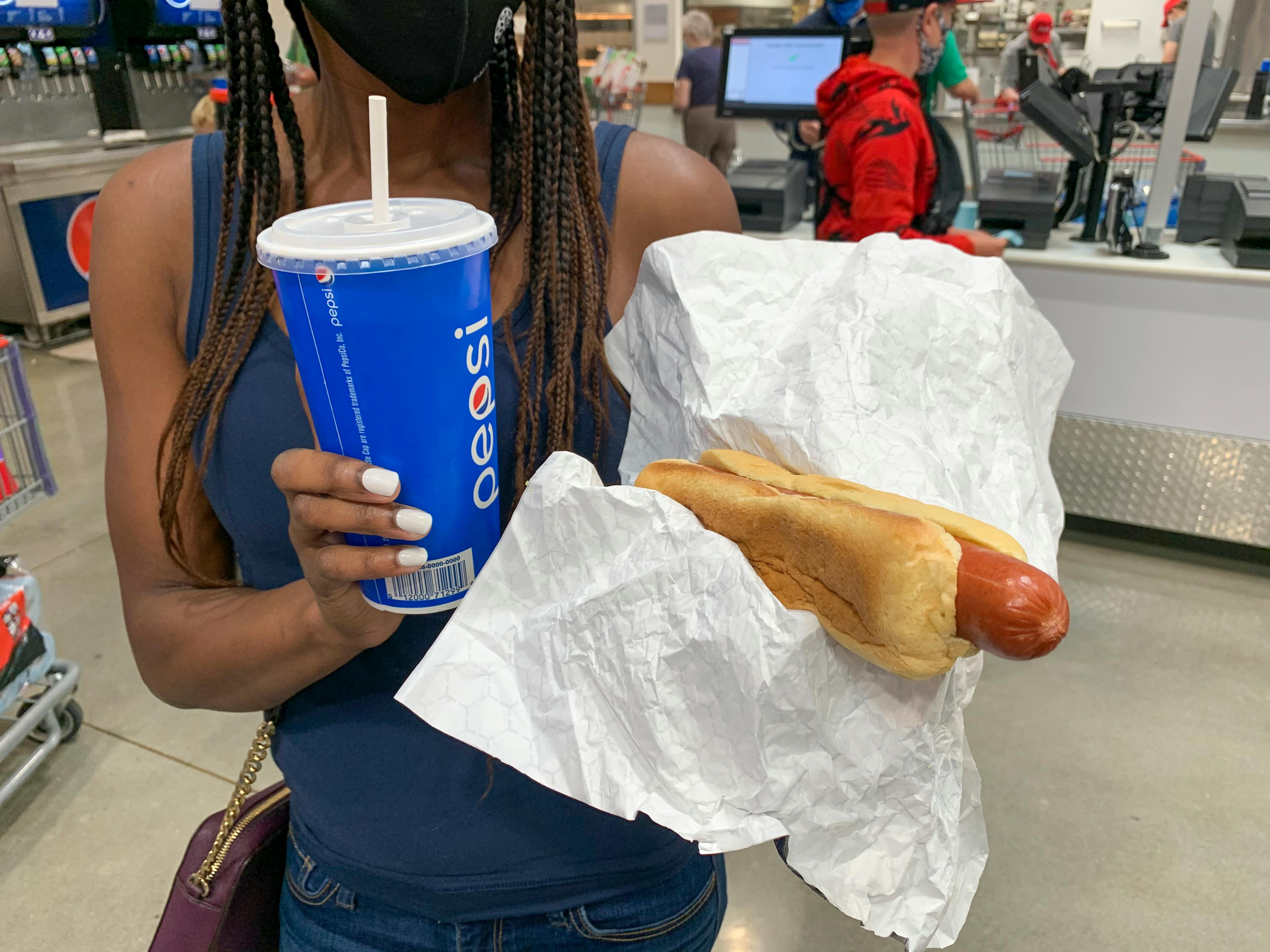 A woman holding a beverage cup and a hotdog near the Costco food court.