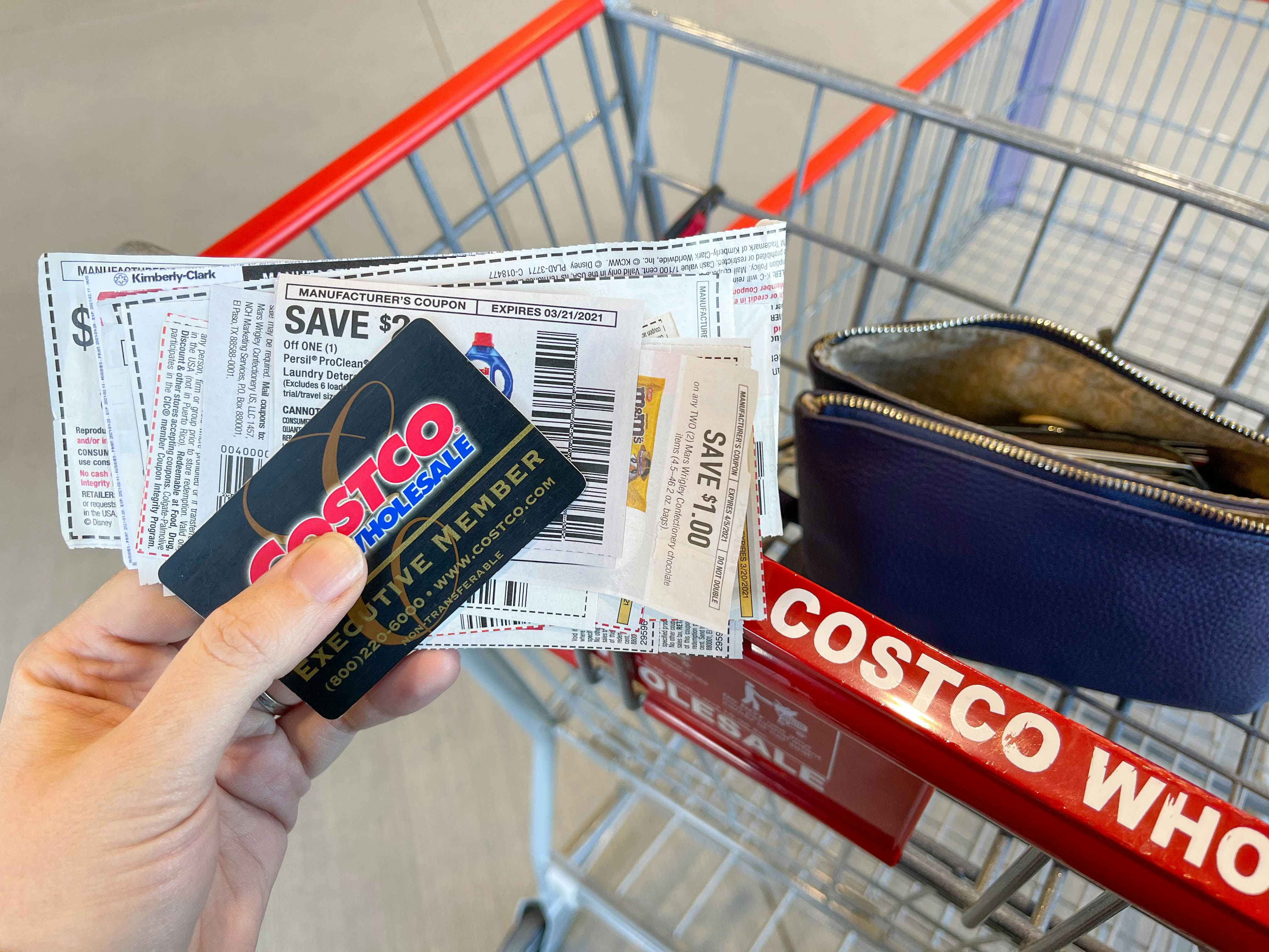 A person holding a costco membership with a stack of coupons