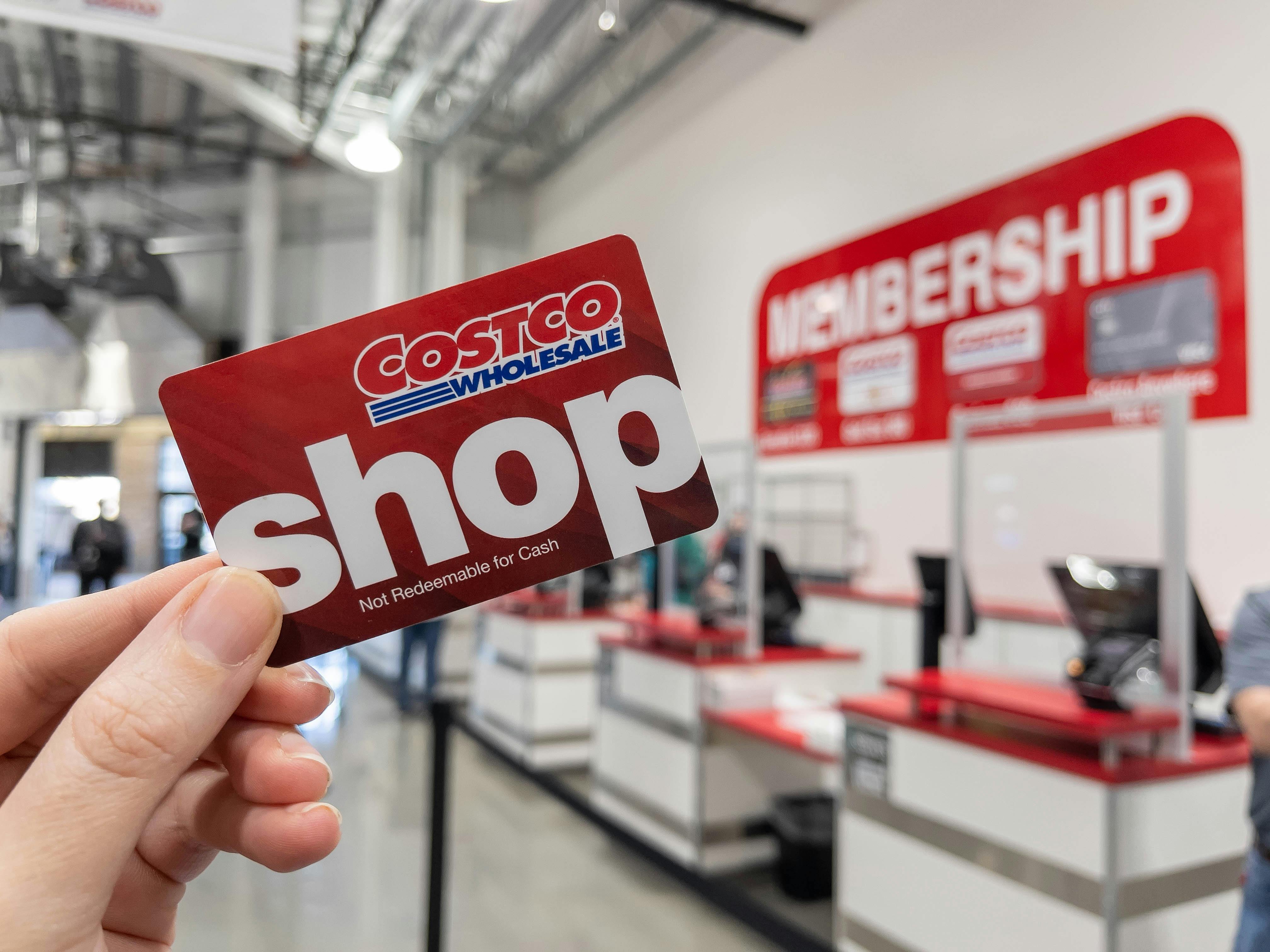 A person holding up a Costco Shop card near the the membership counter.
