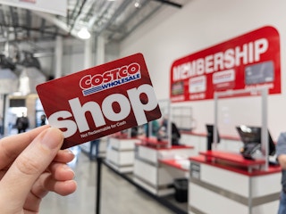 A person holding up a Costco Shop card near the the membership counter.