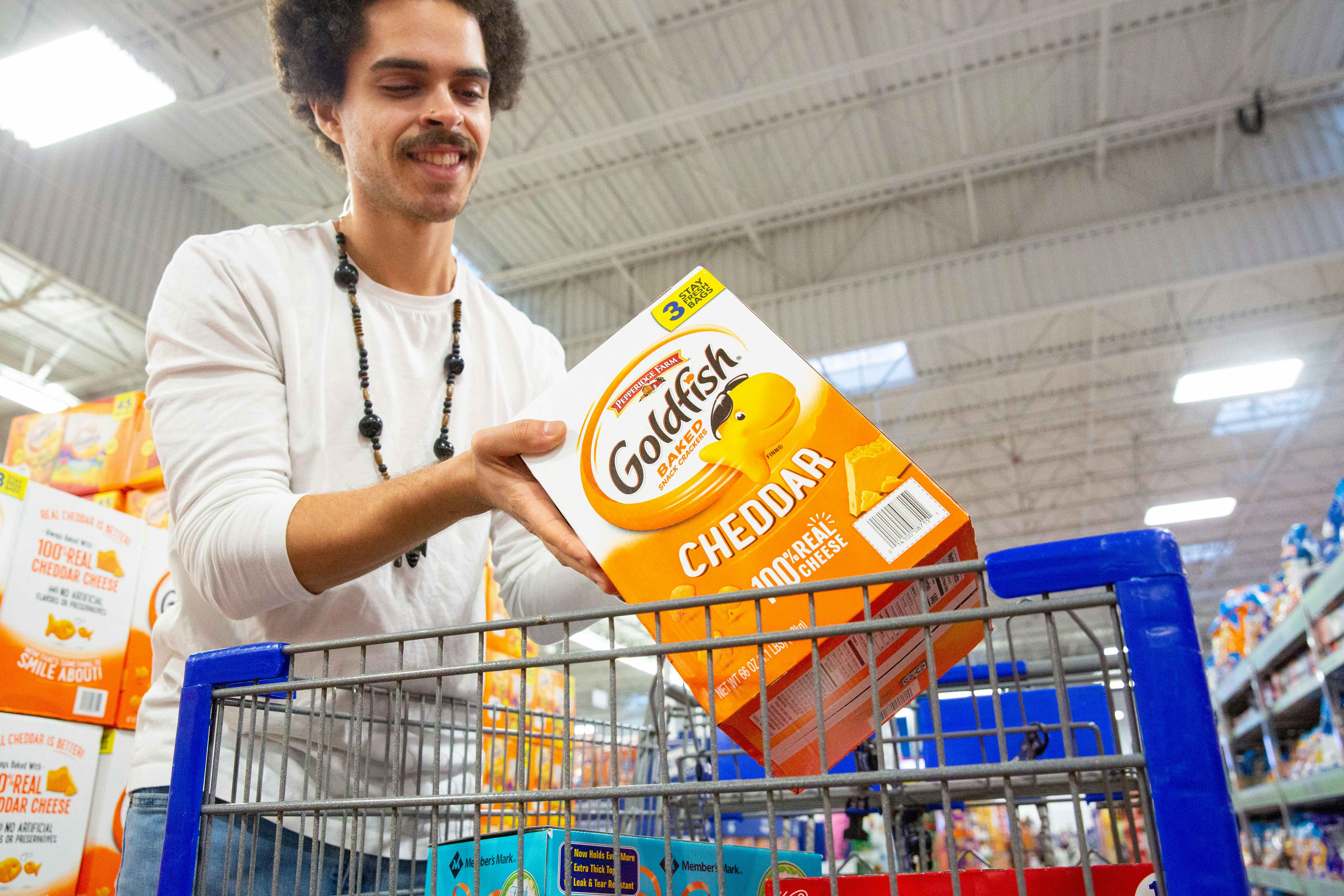 Person placing a bulk box of goldfish crackers into a sam's club shopping cart
