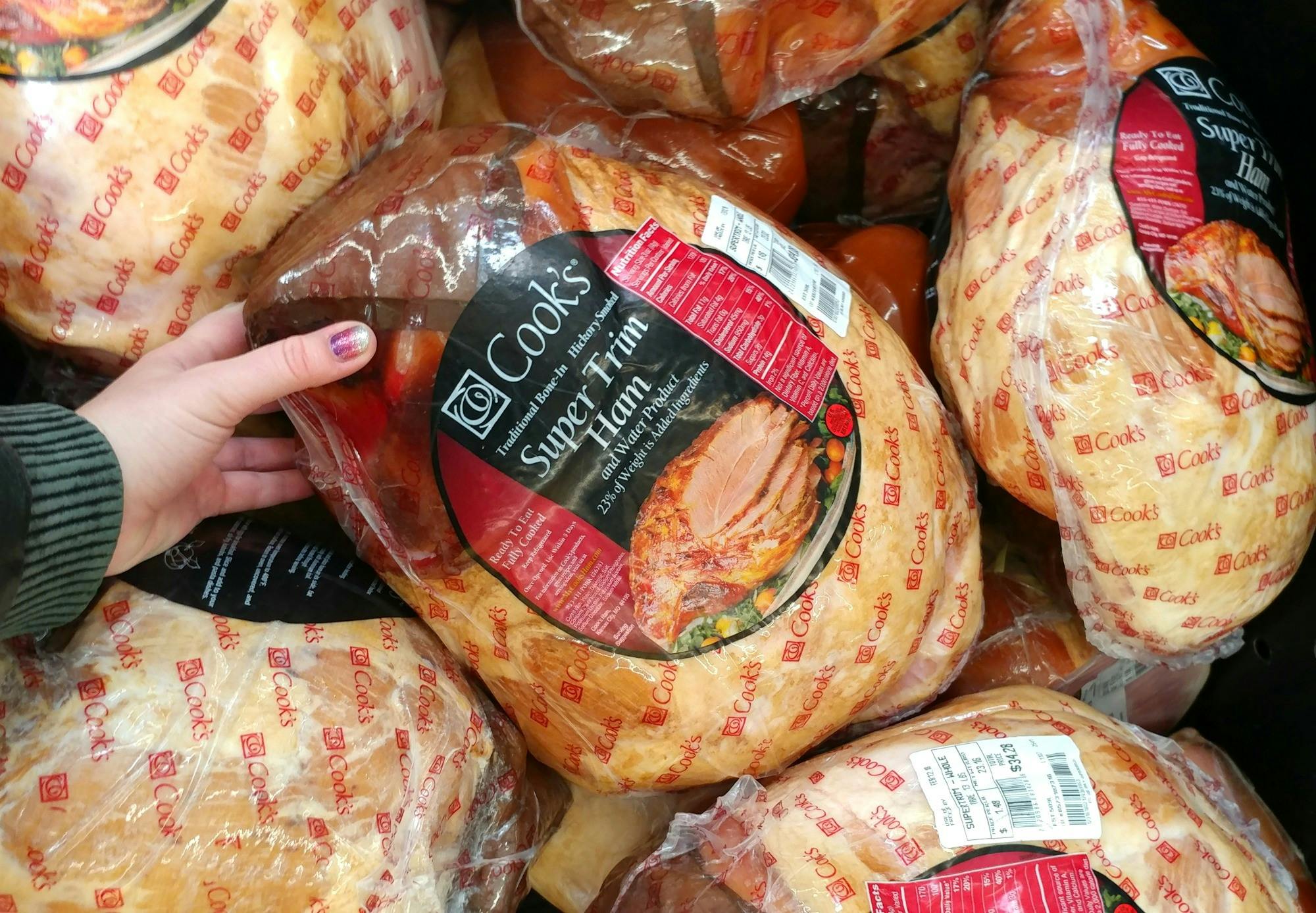 A person holding a Cook's ham in front of a store display case of hams.