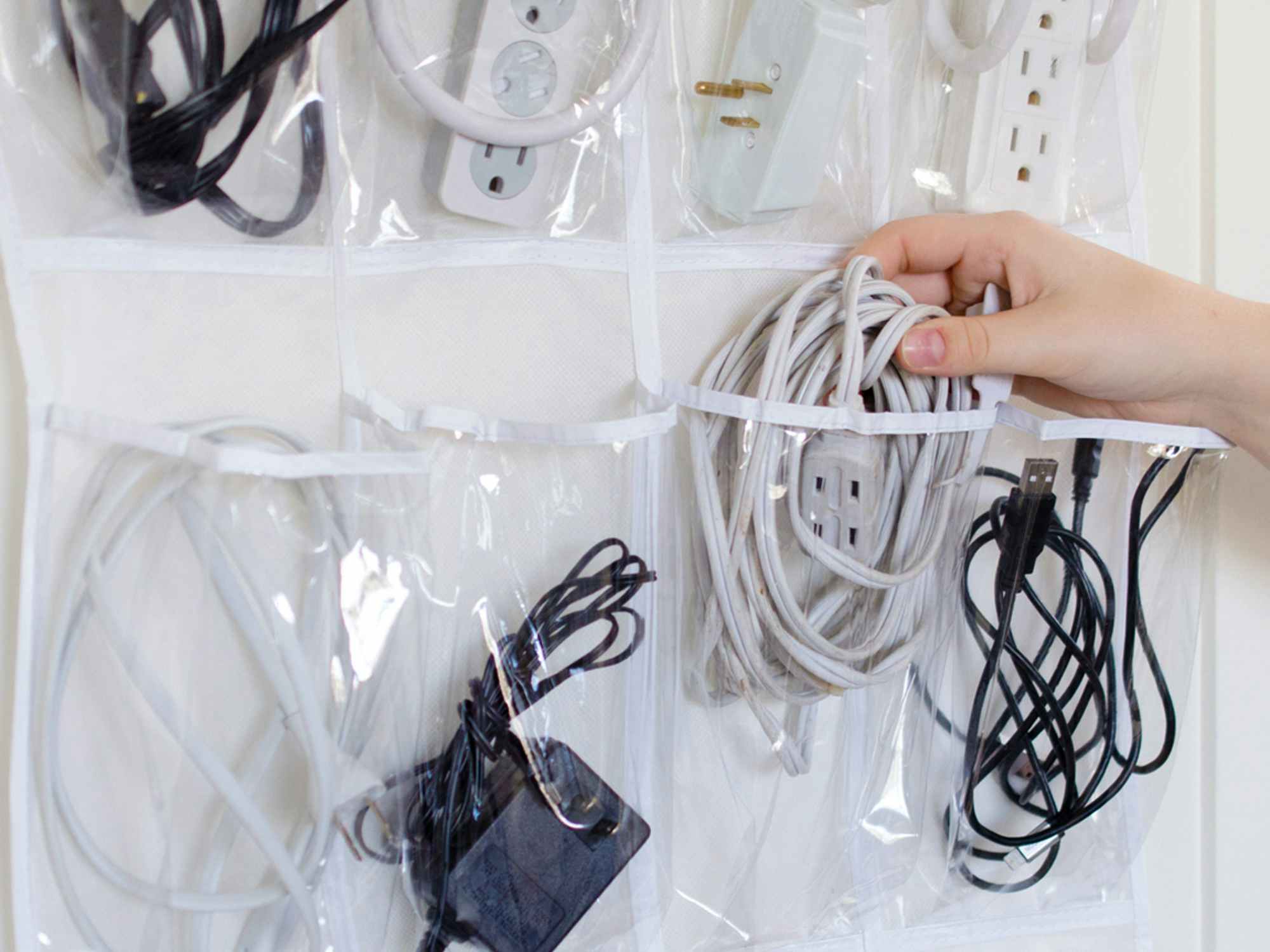 Someone putting an extension cord into a shoe organizer filled with other extension cords and power strips