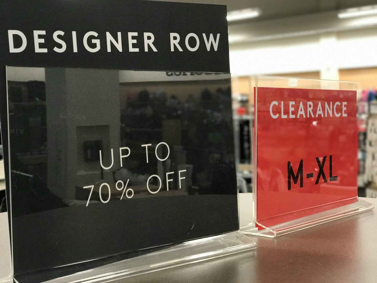 A sign that says "Designer Row" next to a clearance sign on a clothing rack inside Nordstrom Rack.