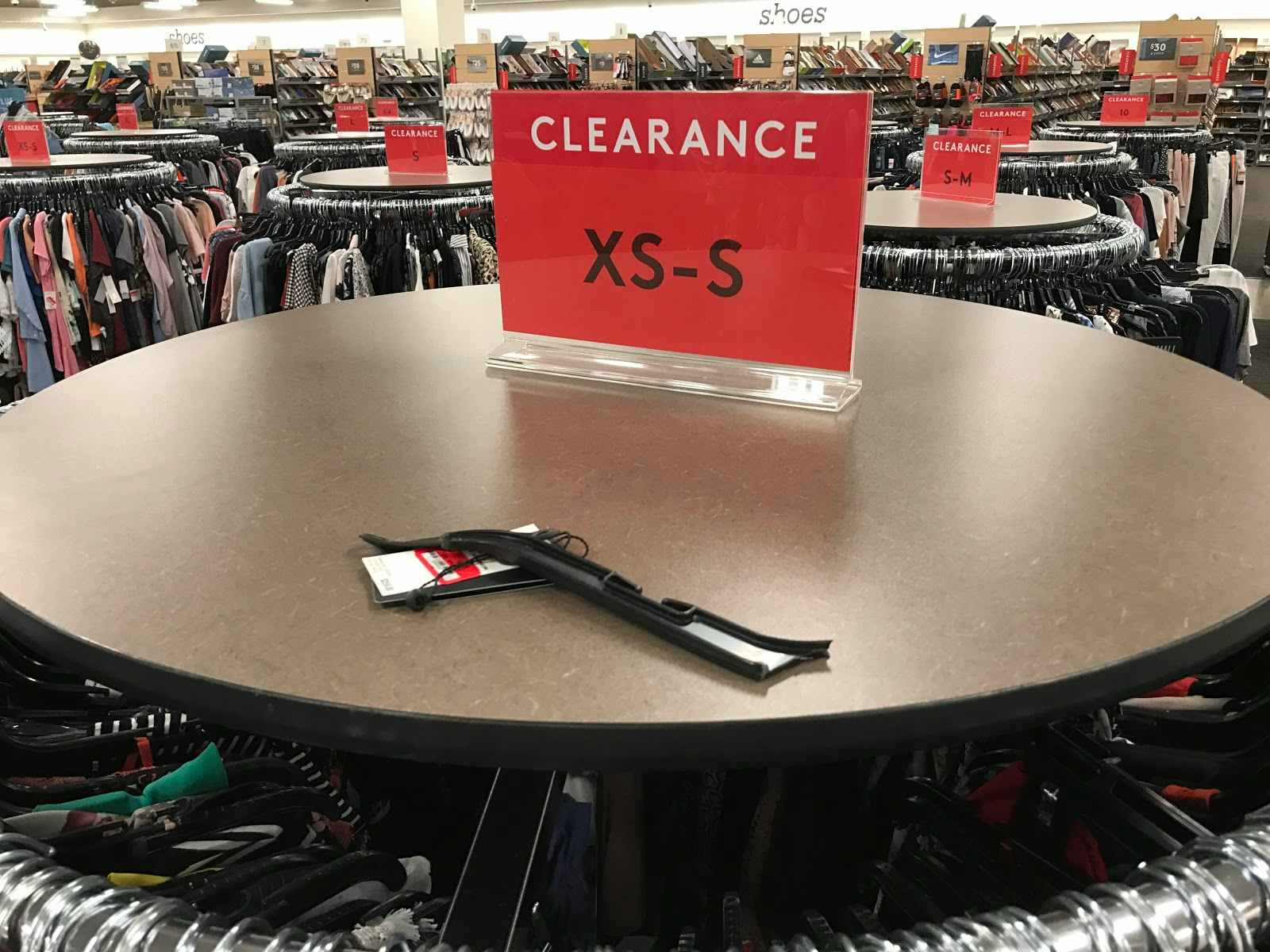 A red clearance sign on top of a clothing rack near the back of a Nordstrom Rack store.