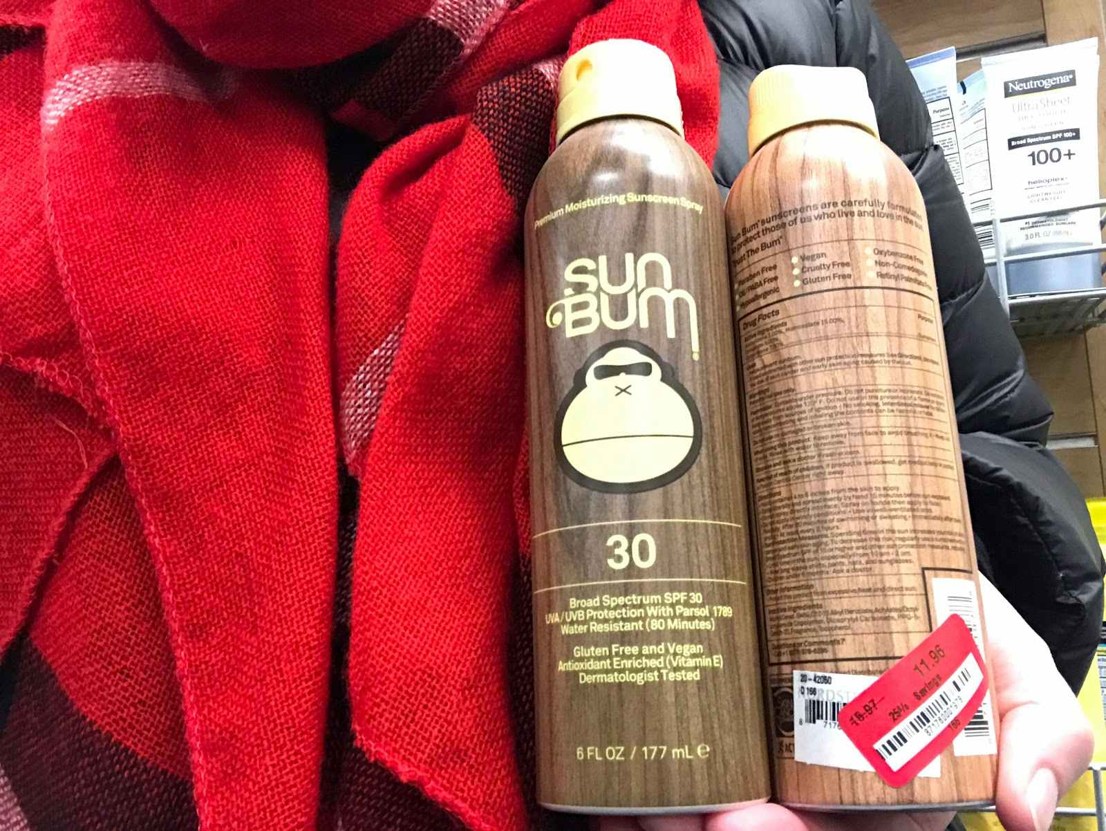 A person wearing winter clothing holding two bottles of Sun bum sun screen. 