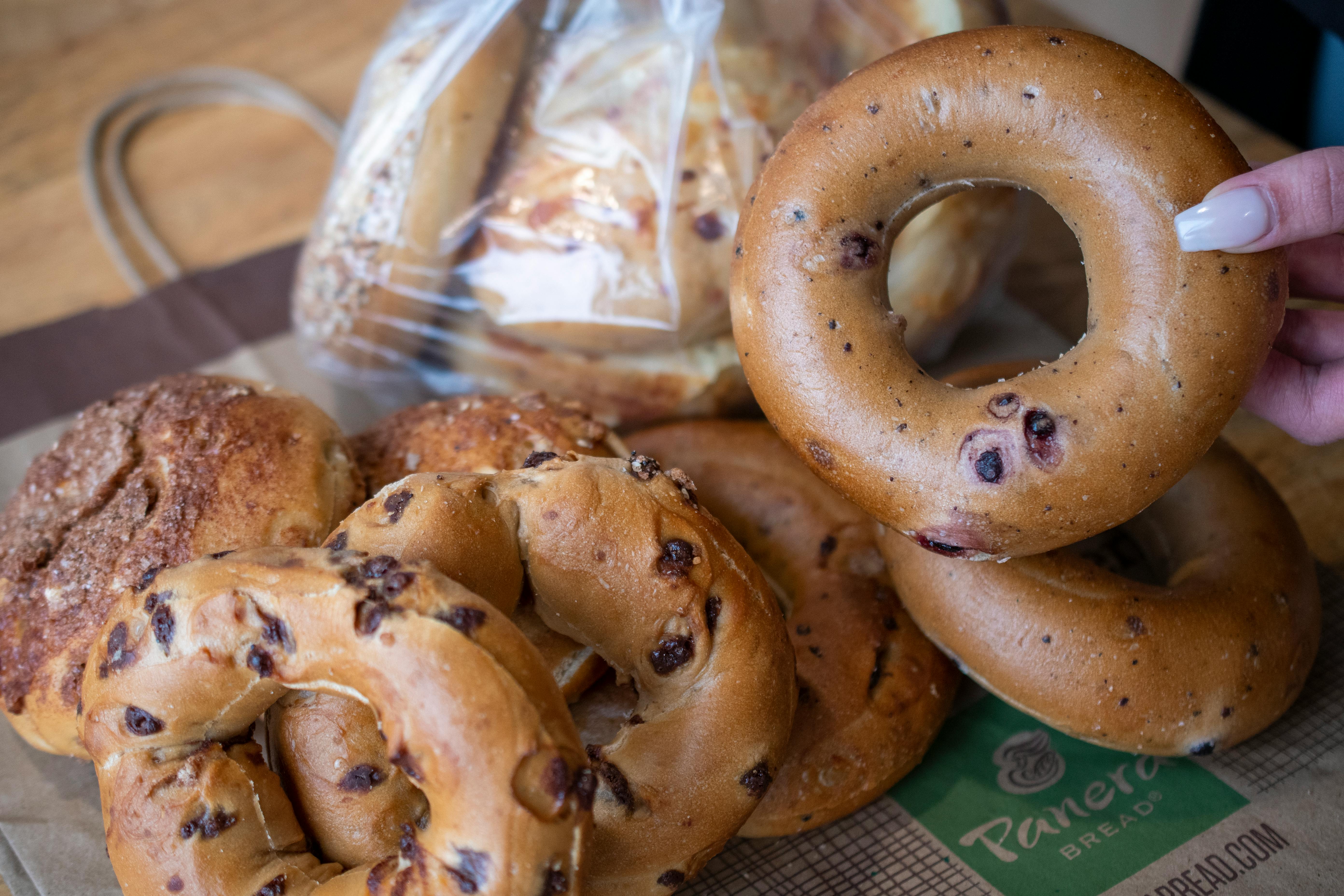 a person holding a bagel with a dozen more sitting on the table beside it.