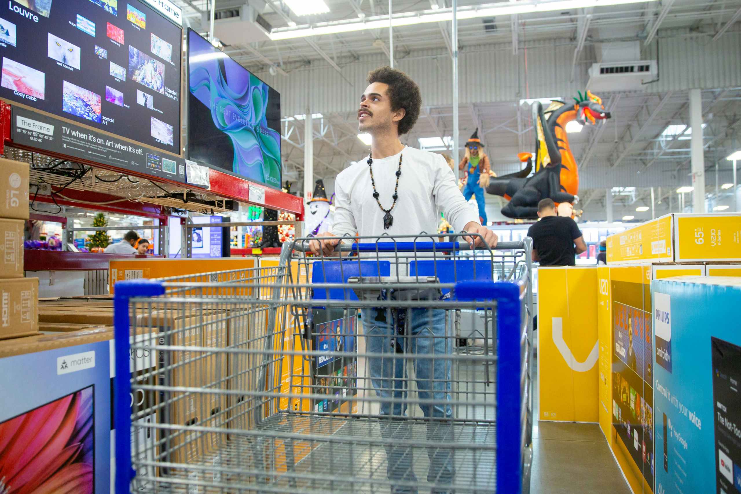 Person pushing a cart while walking inside the Electronics section at Sam's Club