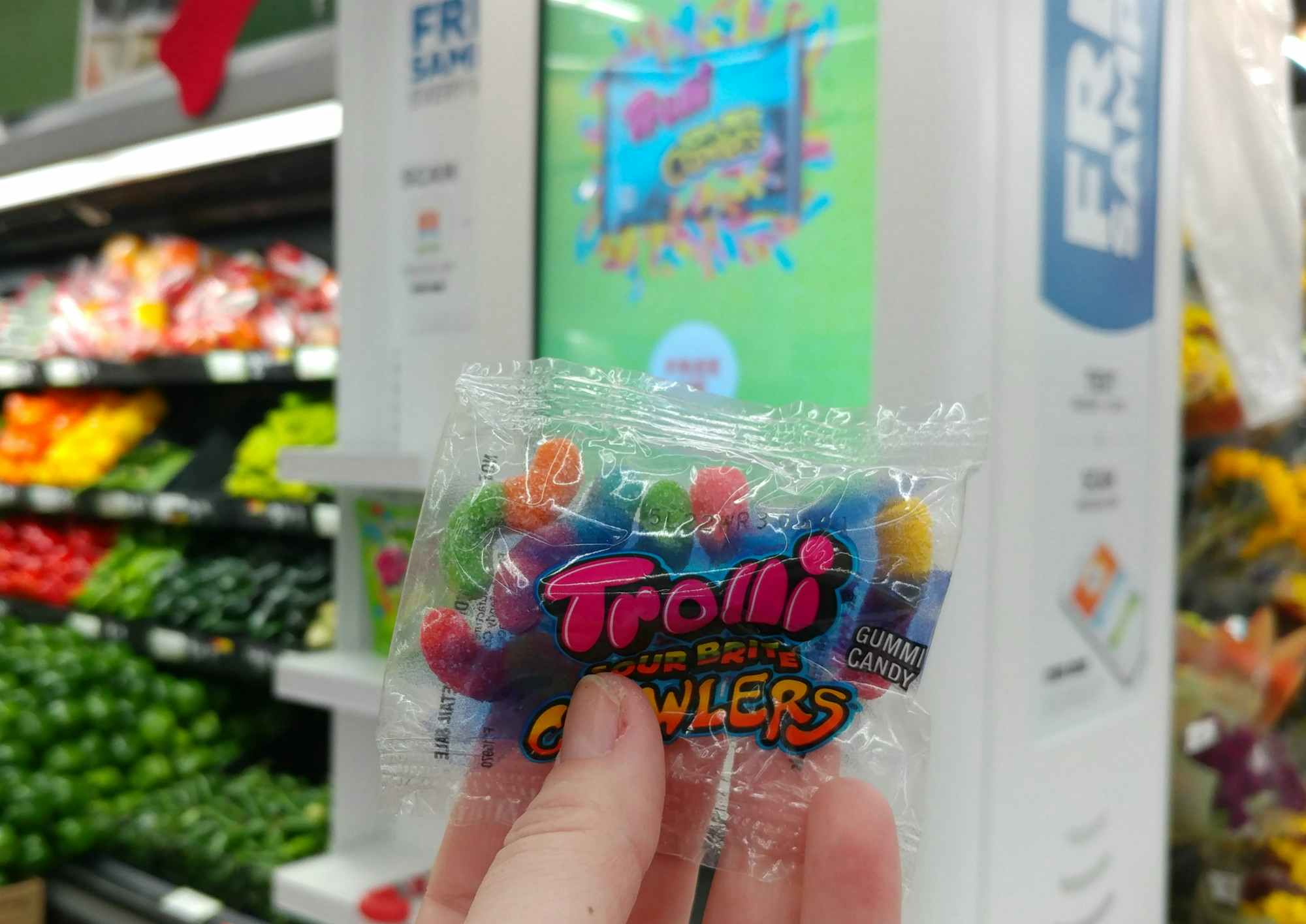 hand holding a sample bag of Trolli candy in front of a Walmart Freeosk