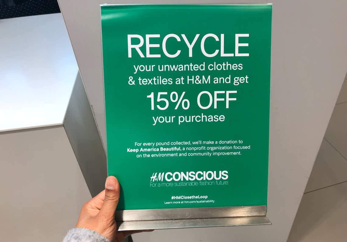 A person's hand holding a sign inside H&M advertising their recycle program.