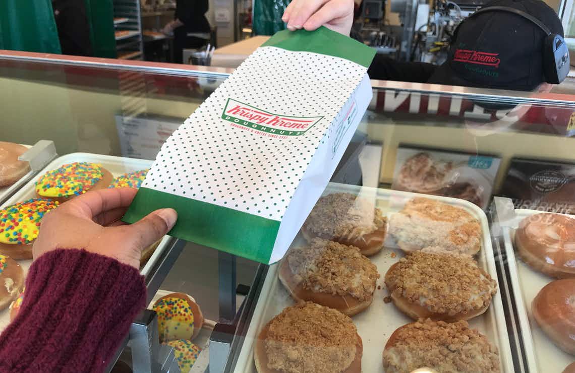 A Krispy Kreme employee handing a bag over the donut display case.