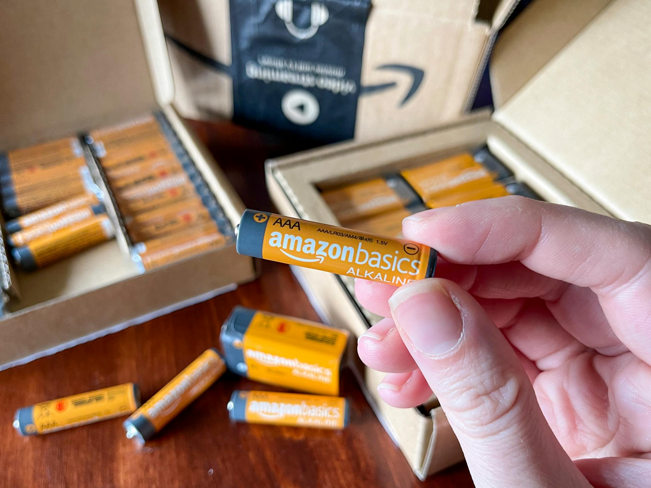 A person holding up an orange amazon basics battery with an open box of batteries in the background.
