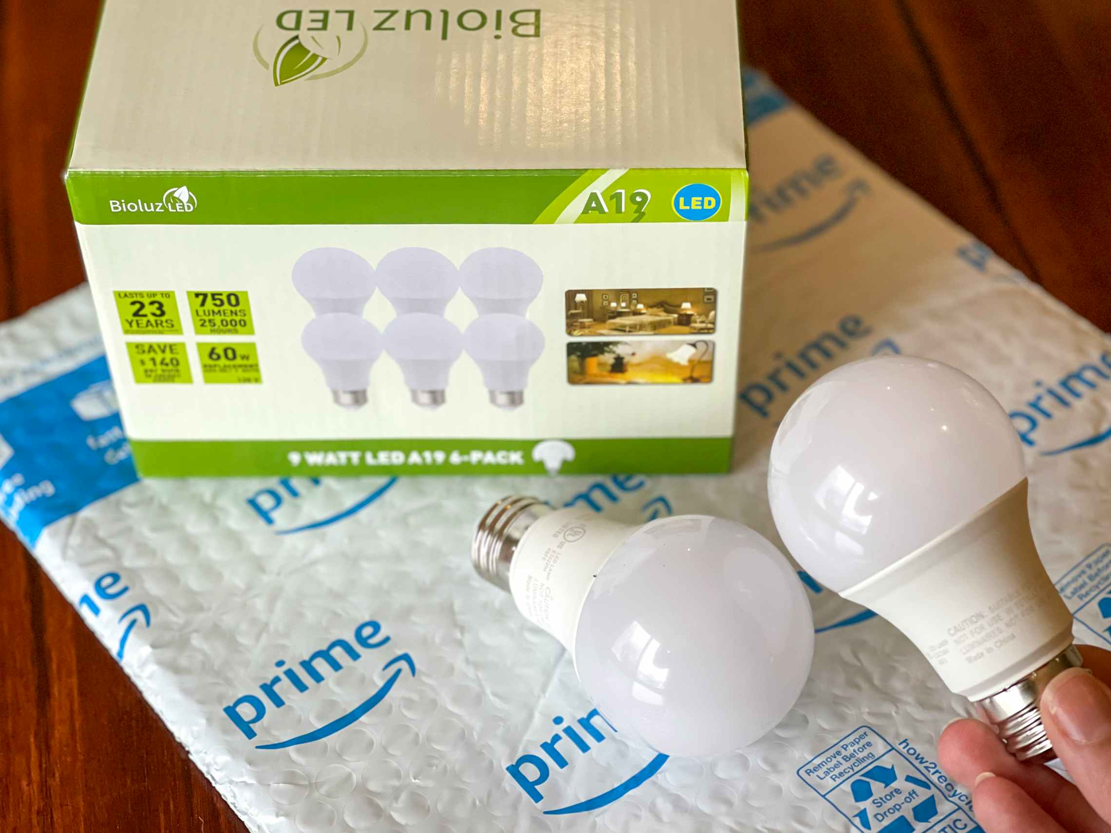 A box of Bioluz LED light bulbs on top of an amazon bubble package, with two bulbs outside of the box, one being held by a person.