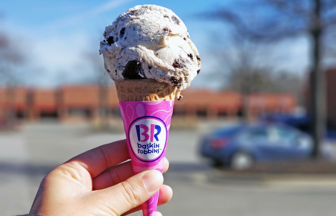 A person's hand holding up a Baskin Robbins ice cream cone.