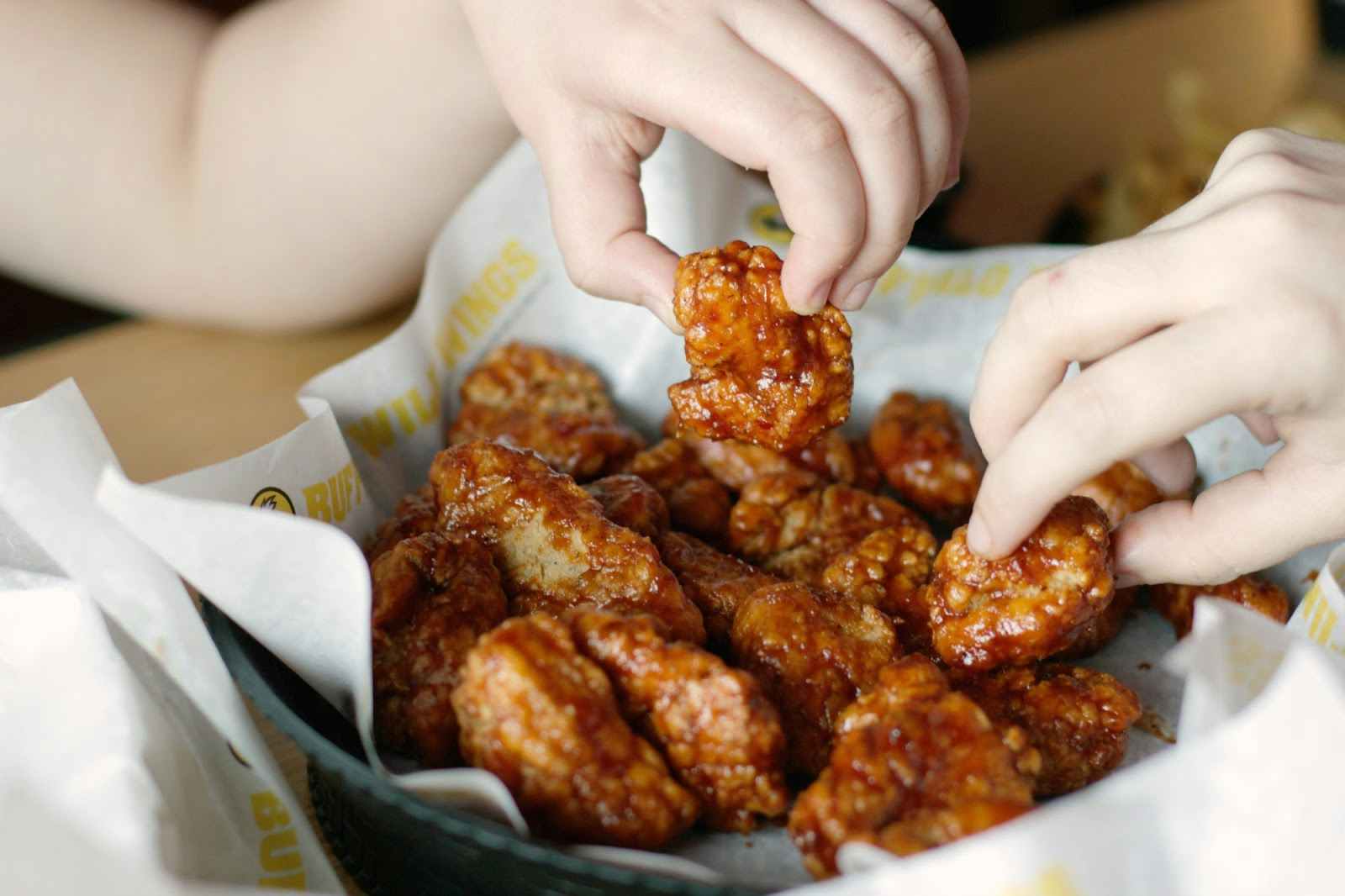 A basket of Buffalo Wild Wings boneless wings sitting on a table with two people reaching in to each take a wing.