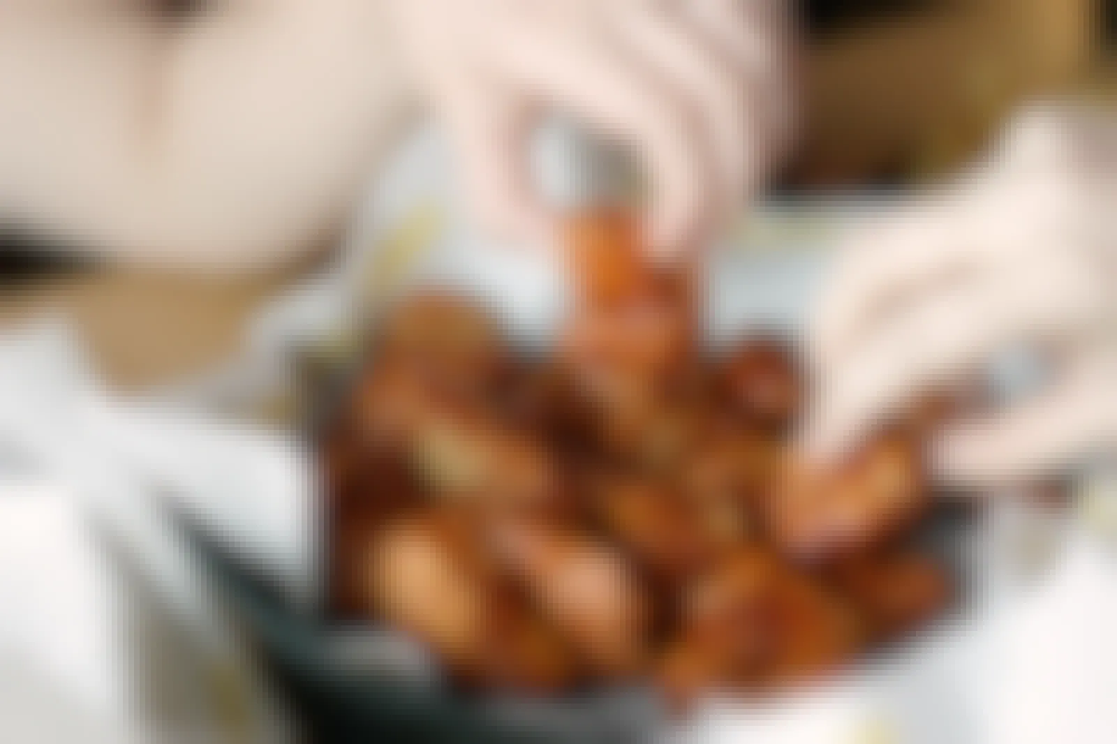 A basket of Buffalo Wild Wings boneless wings sitting on a table with two people reaching in to each take a wing.
