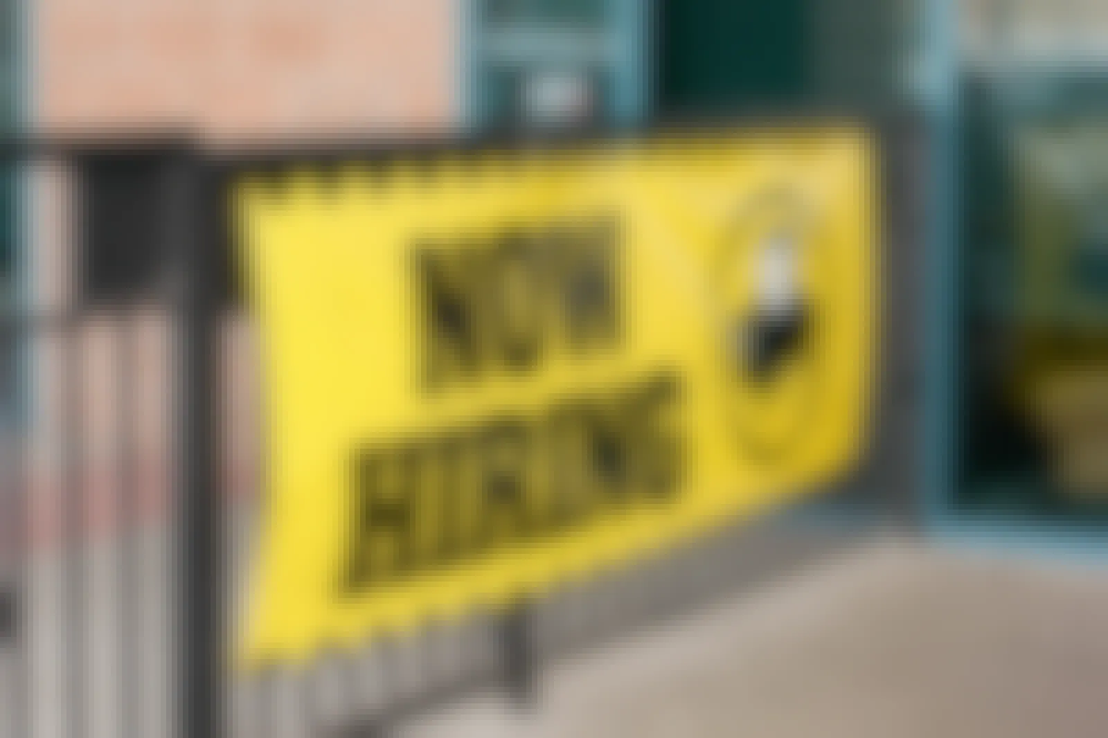 A bright yellow sign affixed to the fence outside of Buffalo Wild Wings which reads 