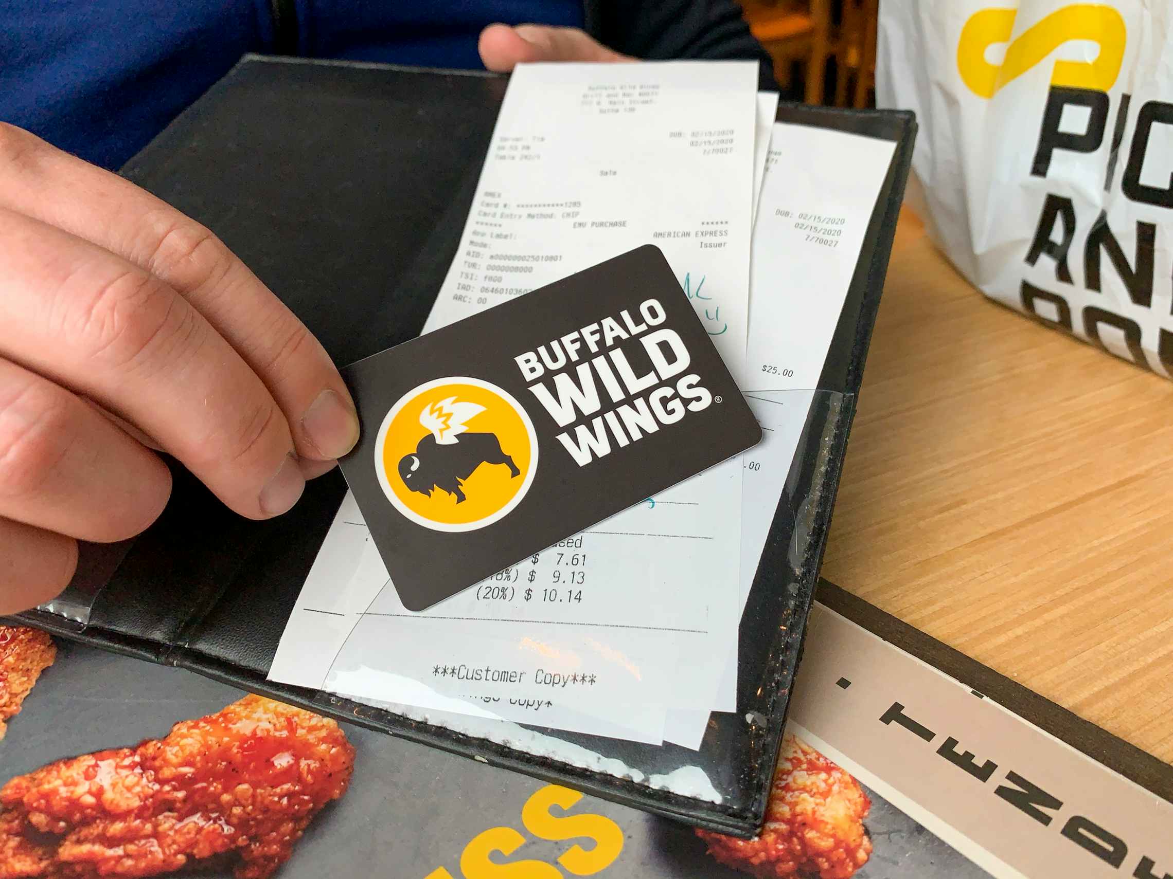 A person placing a Buffalo Wild Wings gift card onto a receipt in a checkout book.