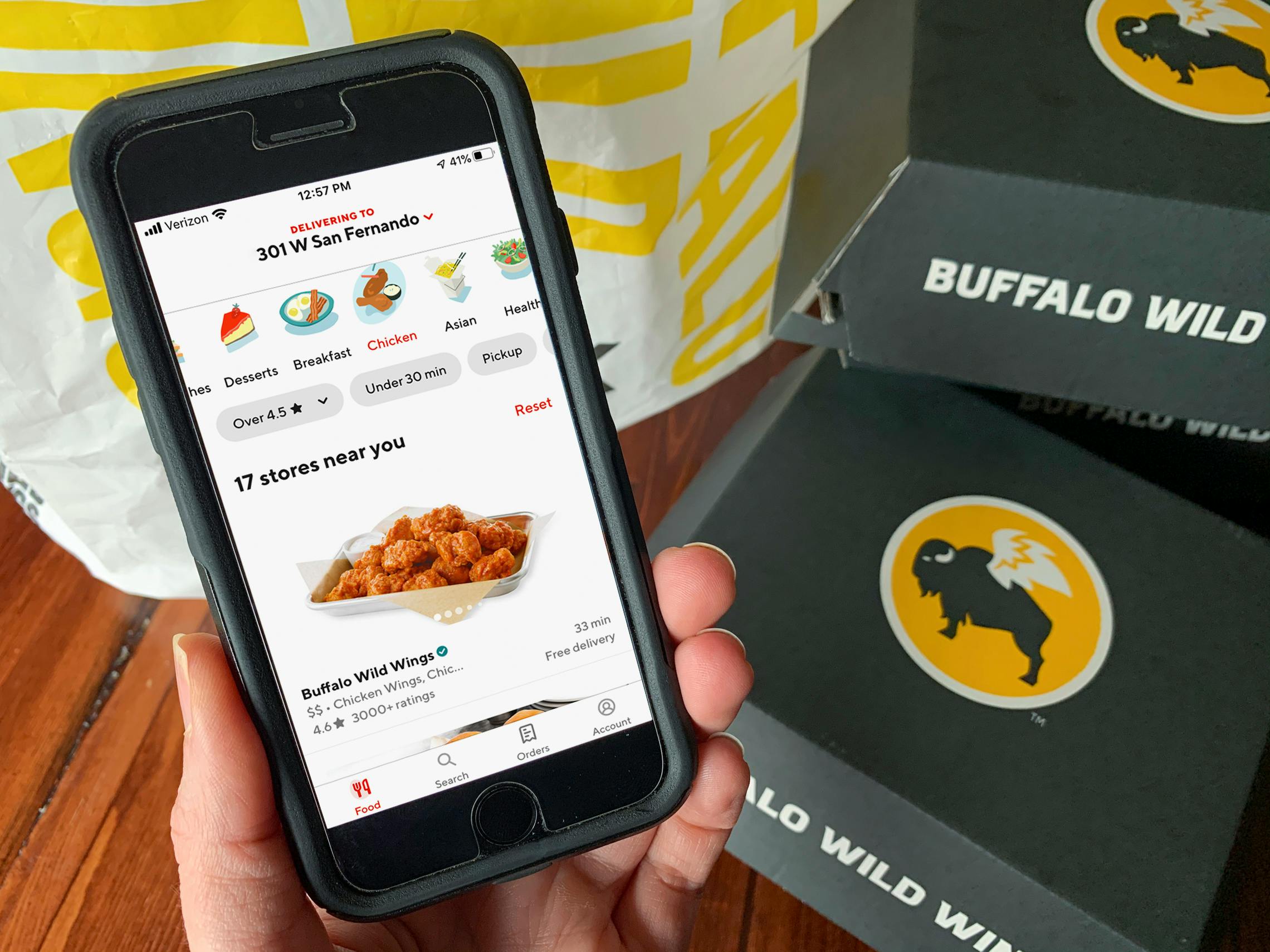 The DoorDash app displaying the Buffalo Wild Wings order page next to to go boxes and a delivery bag.