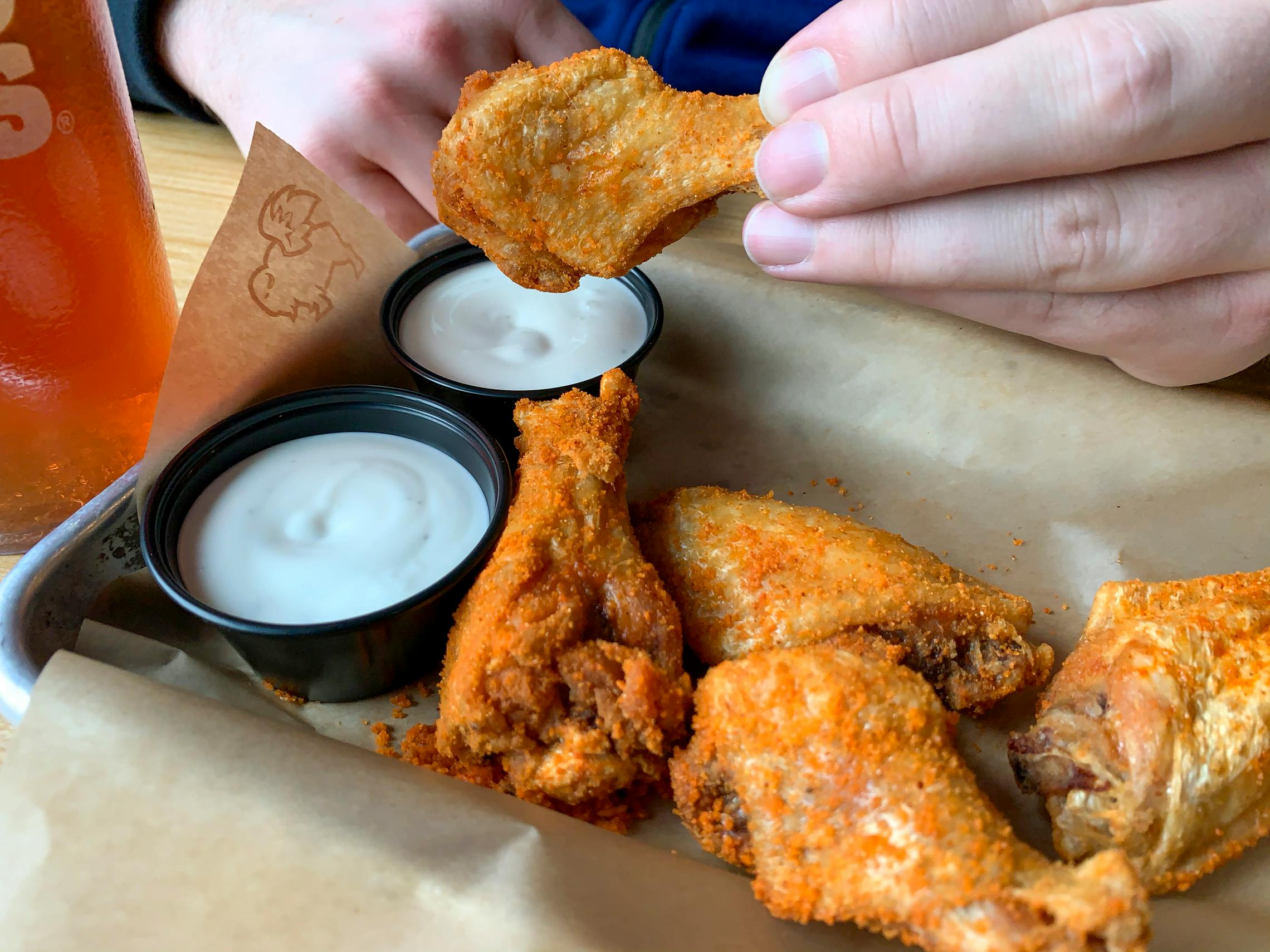 A dry rub seasoned traditional buffalo wings being dipped into ranch dressing, something to enjoy during Chicken Wing Day Buffalo Wild Wings.