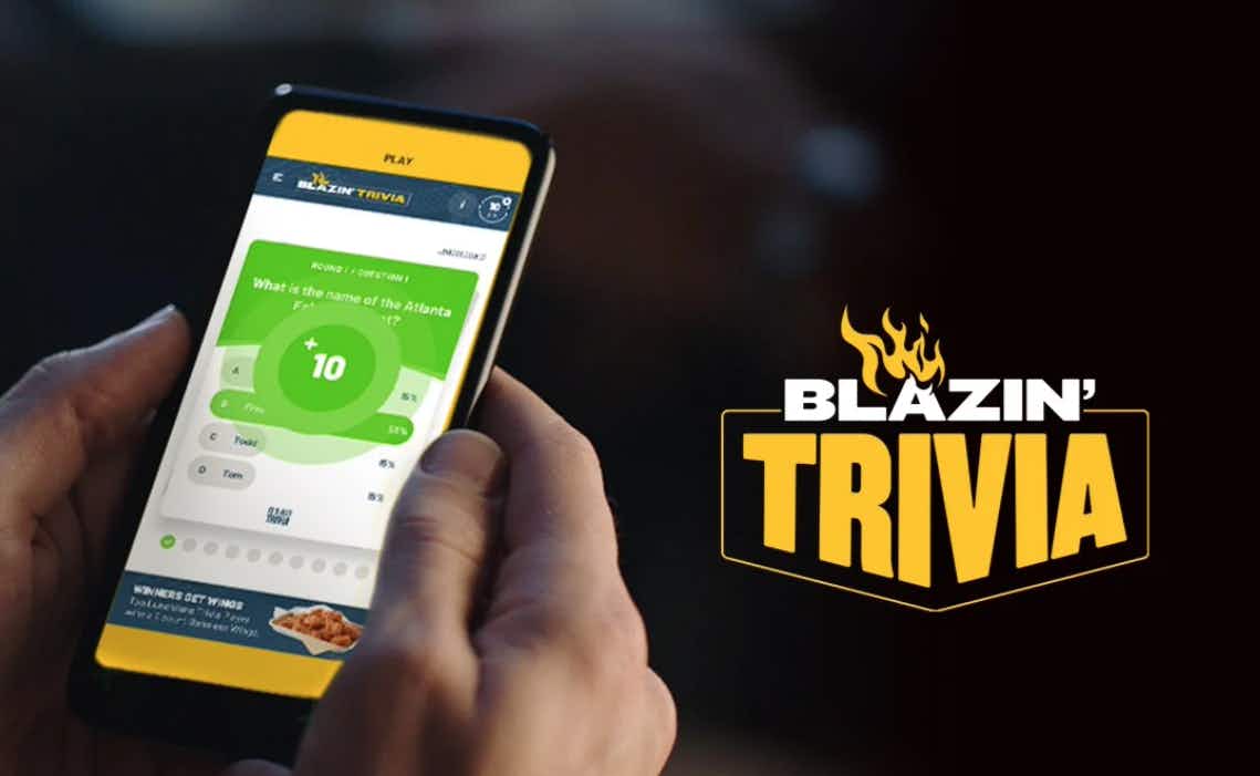 A person holding their phone with the Buffalo Wild Wings mobile app open to the trivia page. The logo for Blazin' Trivia is shown to the right of the phone.