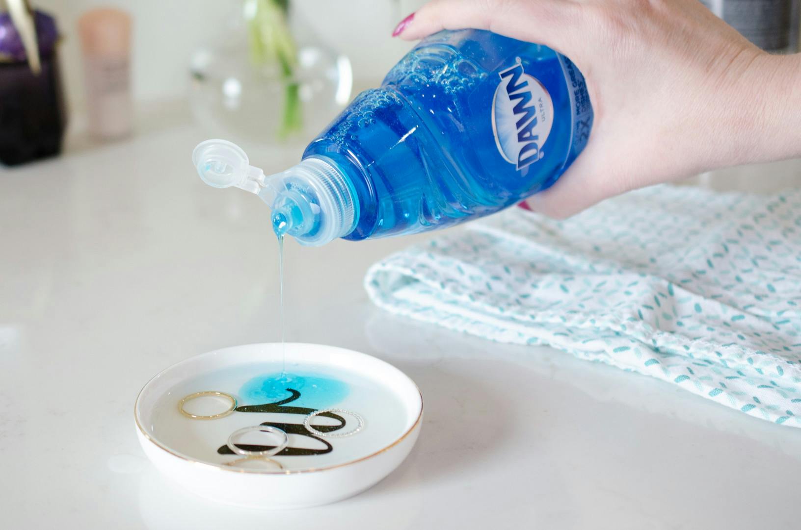Person pouring Dawn dish soap into a bowl with jewelry