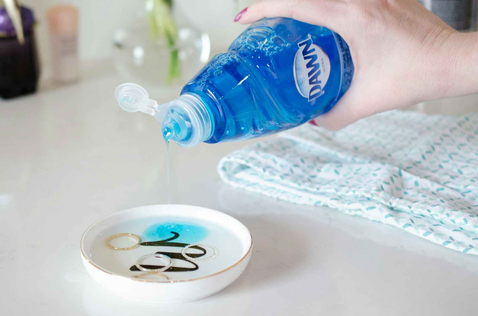 Woman adding drops of Dawn Dish Soap to a small dish with water and rings