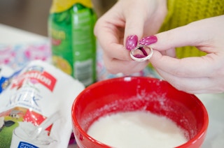 Woman holding a ring over a bowl with a paste made of lemon juice, water, and dry instant milk