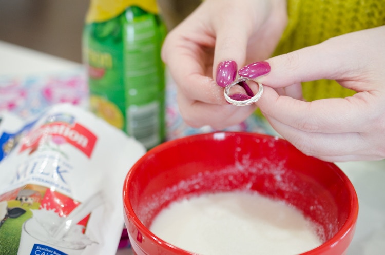 Woman holding a ring over a bowl with a paste made of lemon juice, water, and dry instant milk