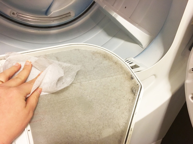 A person wiping out a dryer lint trap with a fabric softener sheet.