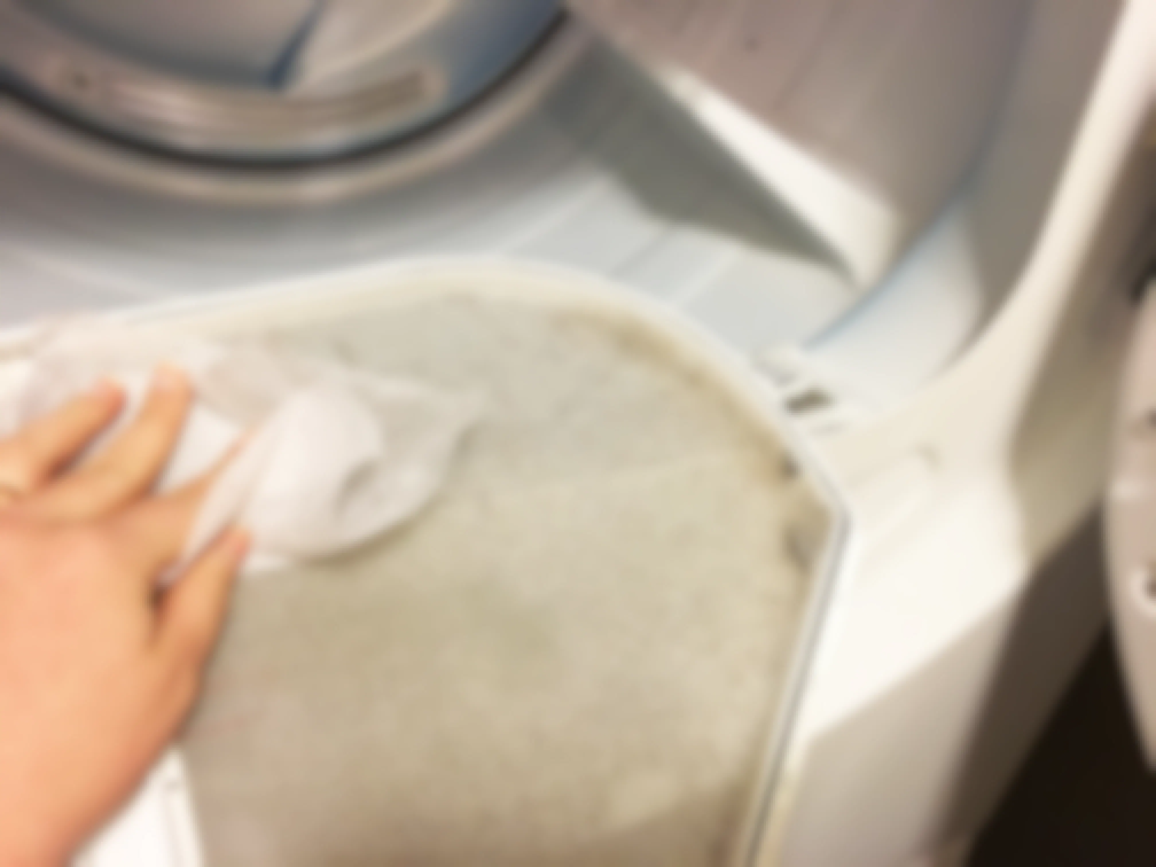 A person wiping out a dryer lint trap with a fabric softener sheet.
