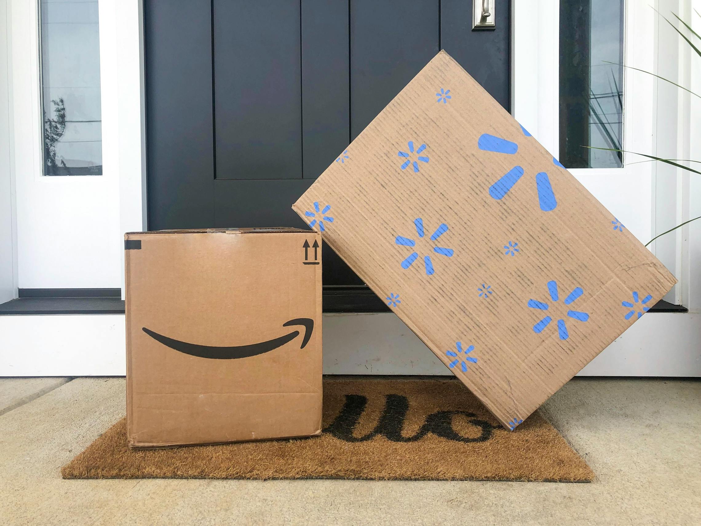 An Amazon and Walmart delivery box sitting on a front doorstep.