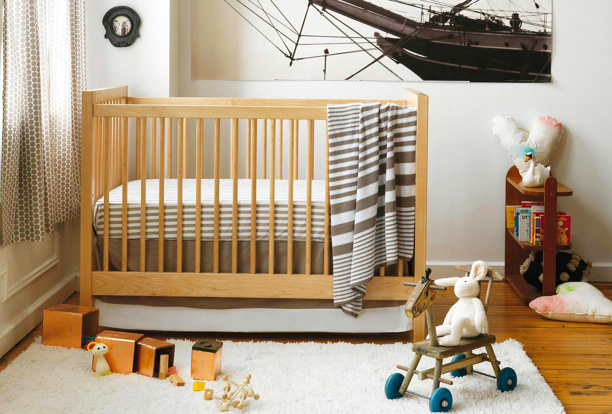 A nursery designed with a Crate & Kids crib and other furniture with some baby toys on a shelf and on the floor.