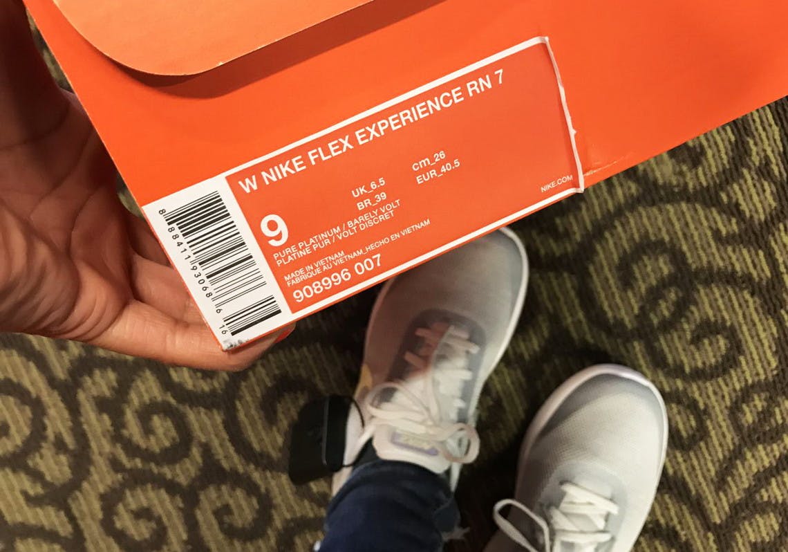 A persons feet with Grey Nike shoes, holding an orange shoebox