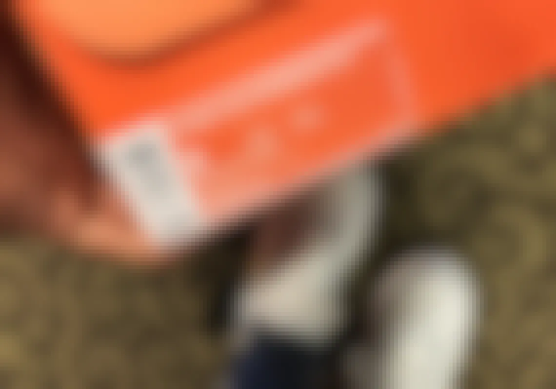 A persons feet with Grey Nike shoes, holding an orange shoebox