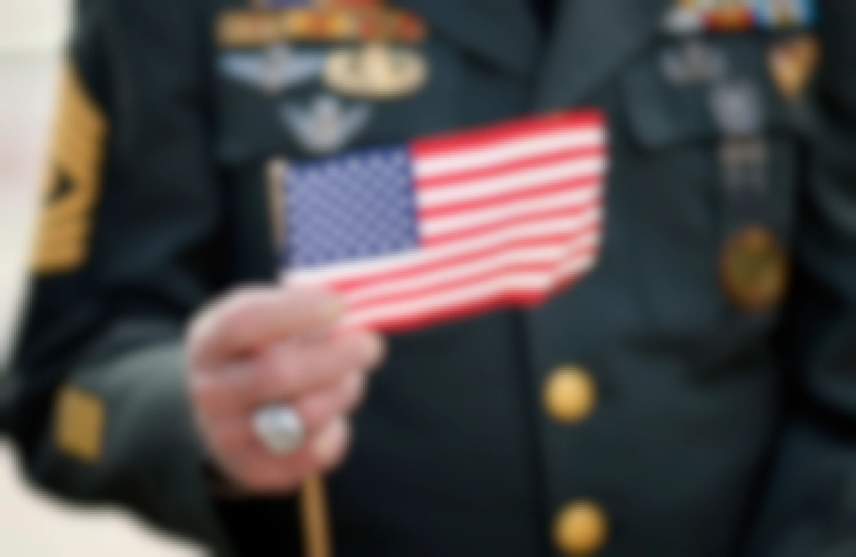 A small American flag being held up by a military veteran in uniform.