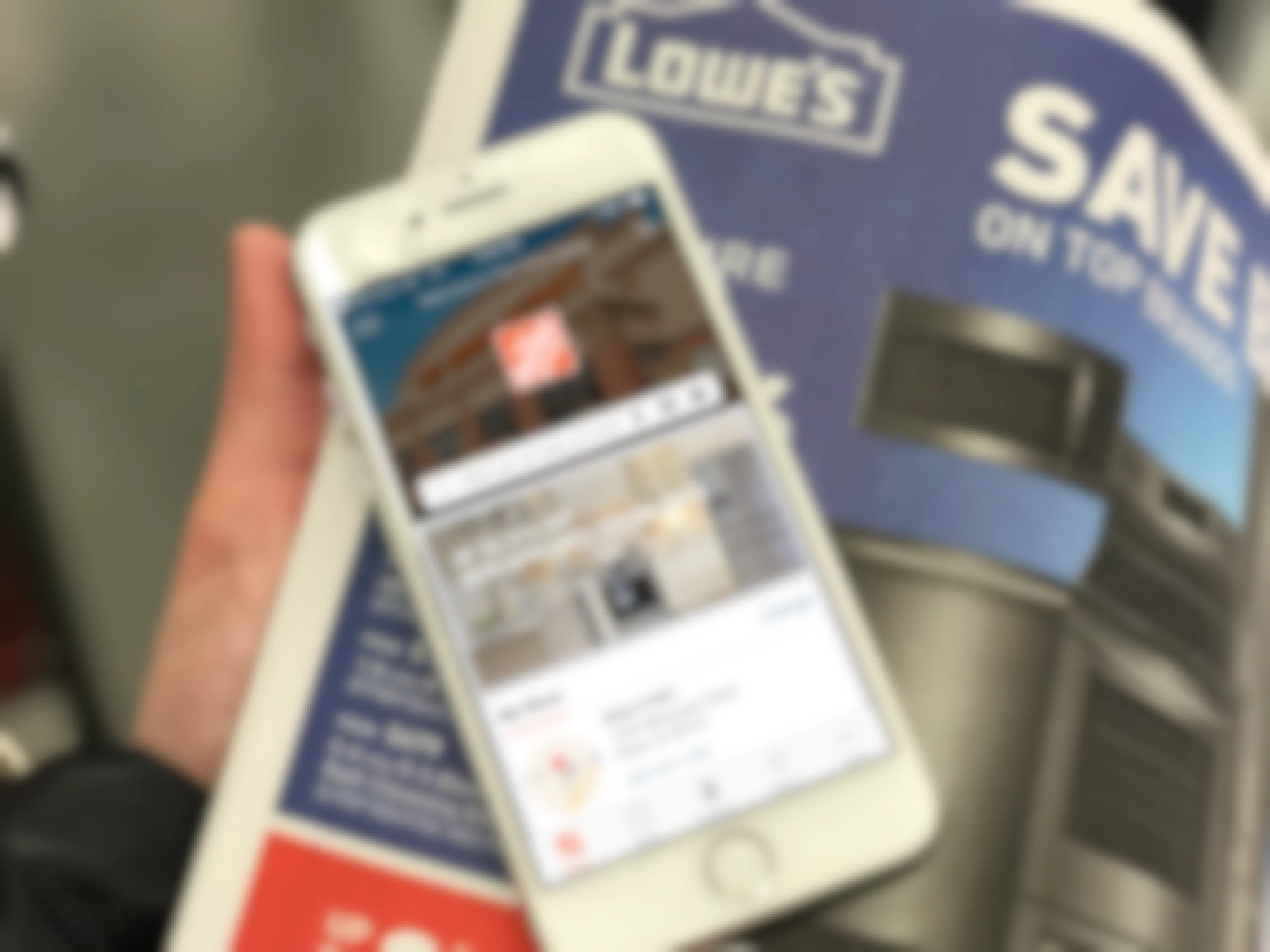 A cell phone displaying The Home Depot app, held on top of a Lowe's weekly advertisement.