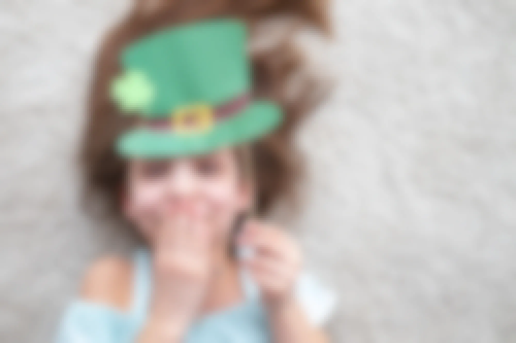 A little girl holding up a leprechaun hat made of construction paper