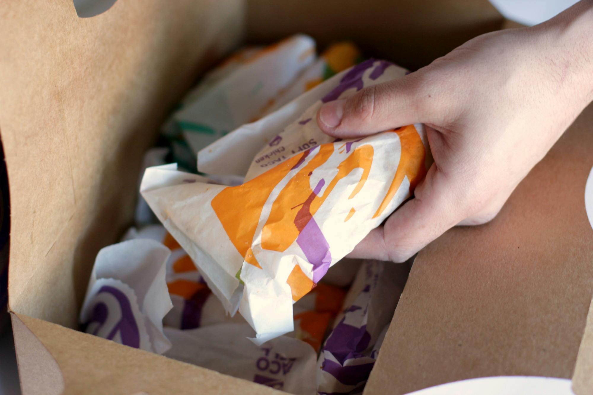 A person's hand taking a wrapped taco from a Taco Bell taco box.