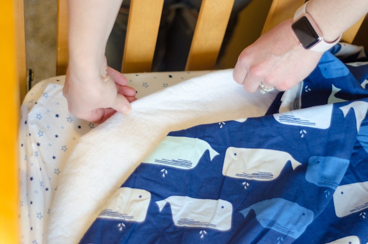 someone pulling a crib sheet off a bed