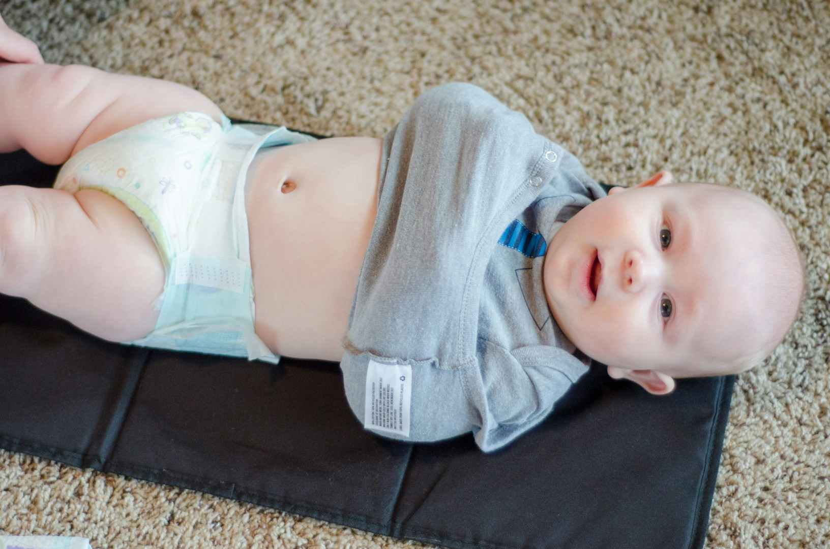 baby on diaper-changing mat with arms tucked in onesie