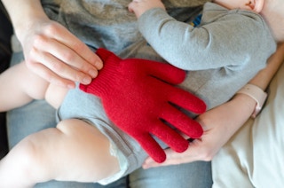 someone holding glove filling with rice on a baby