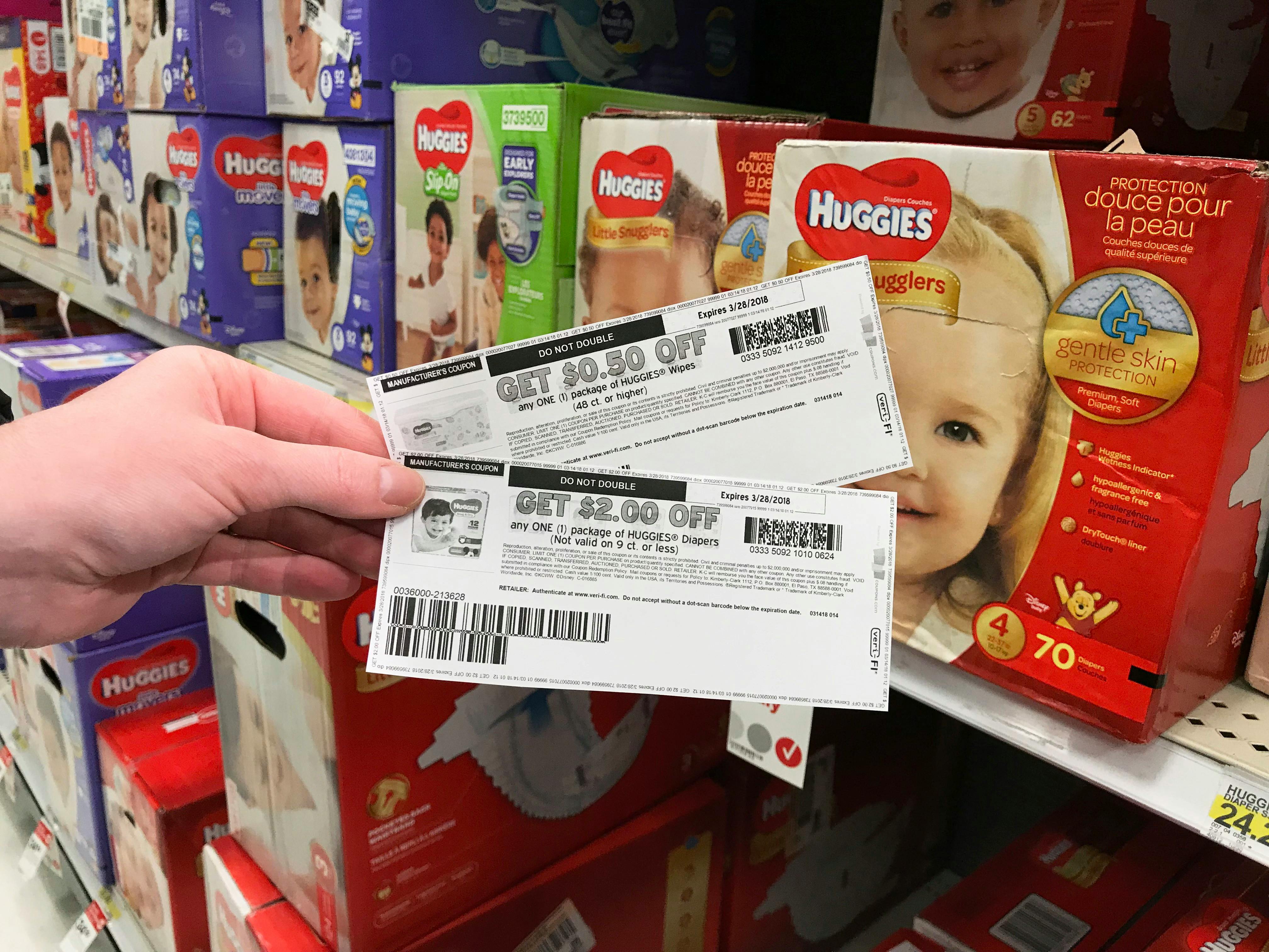 Someone holding coupons in front of Huggies diapers at Walmart