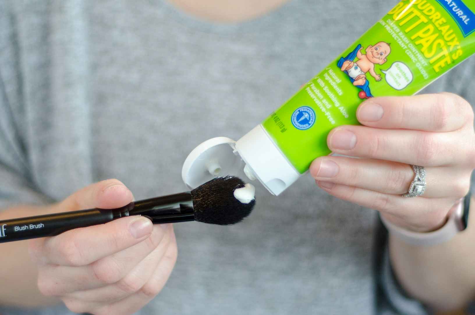 person squeezing baby butt paste onto makeup brush