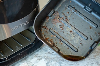 An air fryer with oil and food caked on the bottom of the pan
